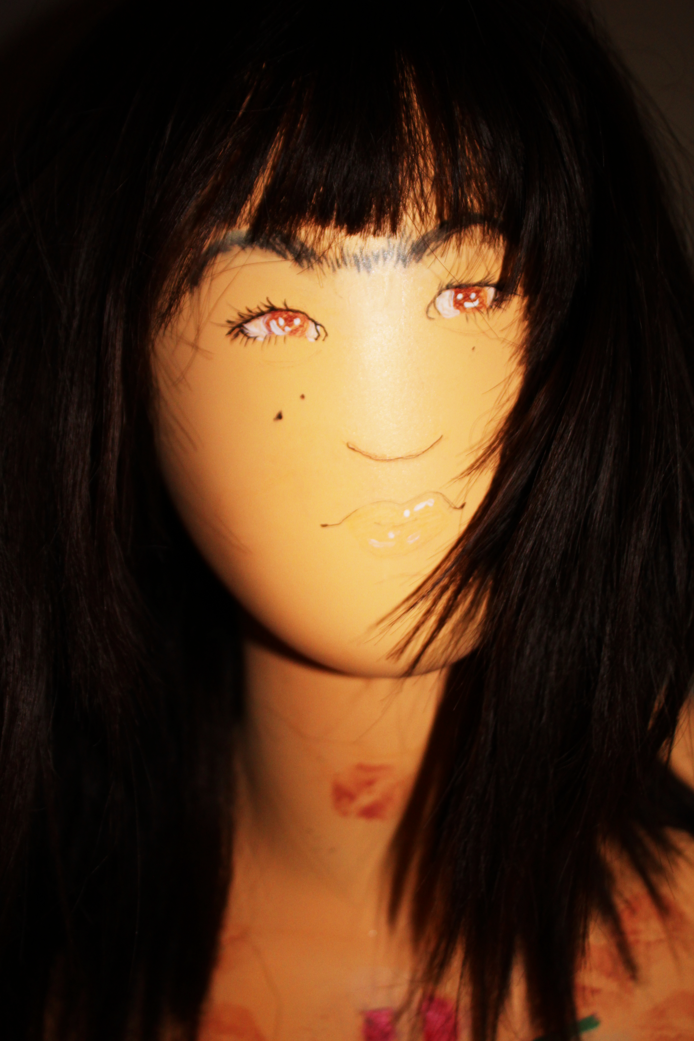 A photo of a young feminine man with long brown hair, a fringe, and a uni brow, he has lipstick marks on his neck and is looking at the camera